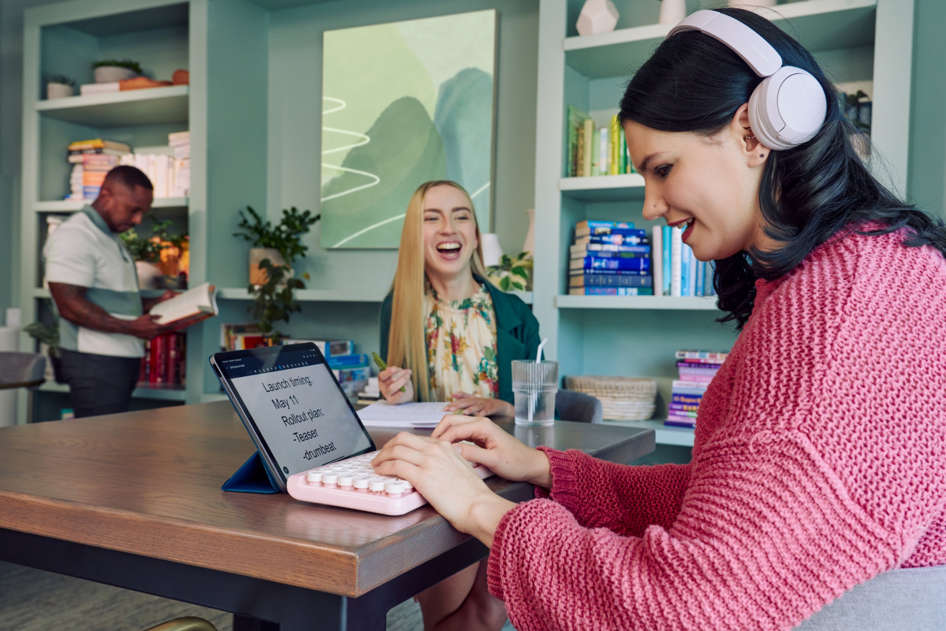 Two colleagues laughing together at a coworking table, one using a tablet and keyboard